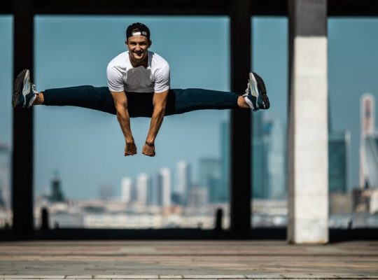 Man performing a split jump on concrete, showcasing fitness and agility.