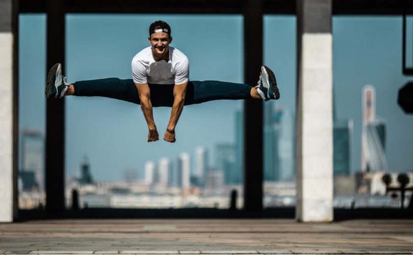Man performing a split jump on concrete, showcasing fitness and agility.